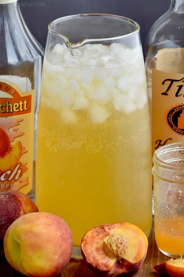 In a large glass pitcher, the Peach Vodka Smash has a golden yellow color with ice cubes. 