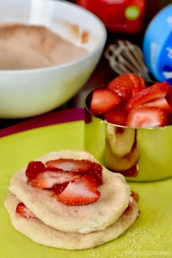 A stack of biscuit dough has sliced strawberries in-between the dough and some sugar