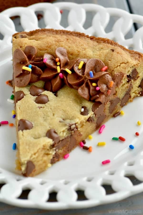 On a white plate, there is a slice of the Chocolate Chip Cookie Cake with chocolate frosting on the edge and rainbow sprinkles. 
