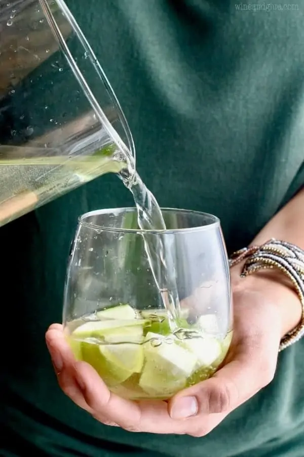 A woman is pouring the Caramel Apple Sangria into a glass cup that has sliced apples inside. 