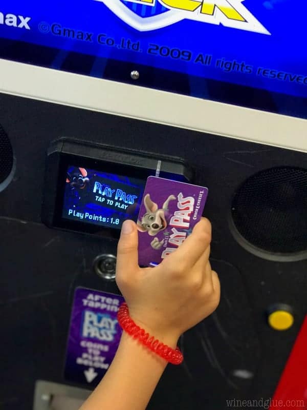 A little girl holding the Chuck E. Cheese's day pass on a game. 
