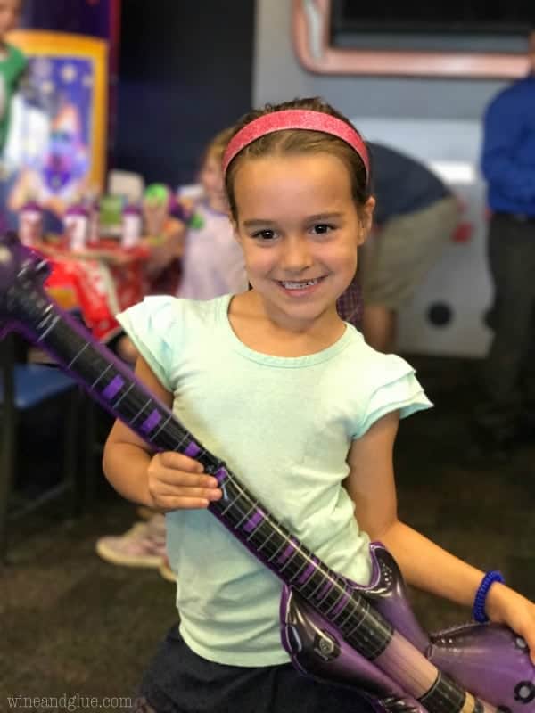 A little girl with a headband holding an inflatable guitar. 