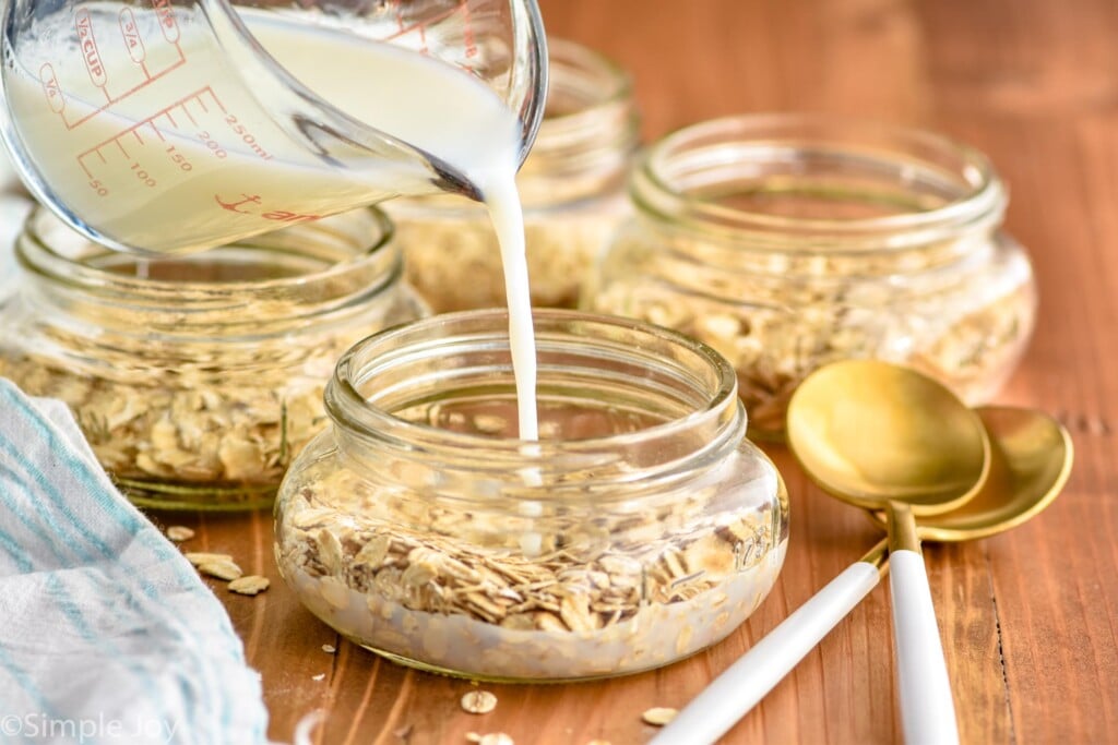 milk being poured into a small mason jar with dry oats in it