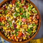overhead view of a wood bowl on a blue wood surface surrounded by tomatoes and chips and with cowboy caviar inside - 15