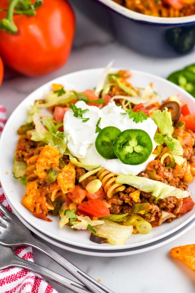 easy taco casserole on a small white plate, topped with sour cream and fresh sliced jalapeños