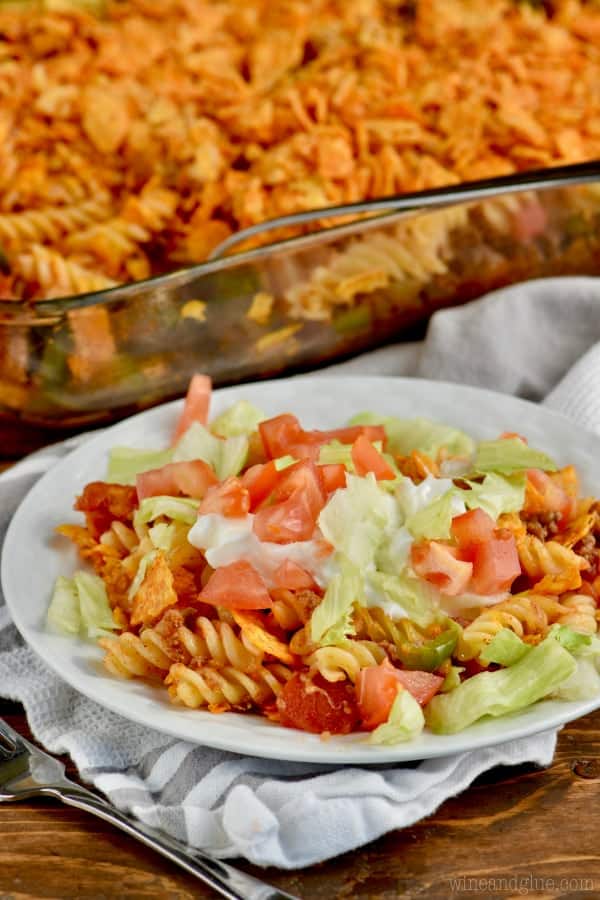 On a white plate, the Pasta Taco Casserole is topped with lettuce and tomatoes. 