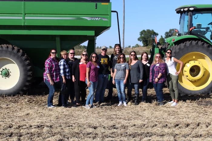 A group photo of people on a field right in front of a tractor. 