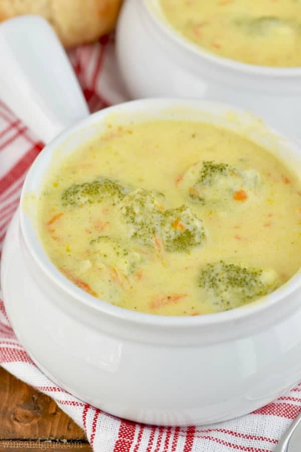 In a small white bowl with a handle, the Broccoli Cheddar Soup has speckles of green from the broccoli and carrots. 