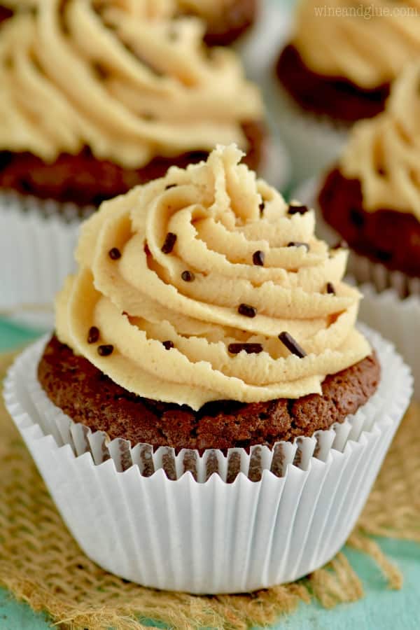 In white cupcake liners, are the Chocolate Peanut Butter Brownie Cupcakes topped with Peanut Butter frosting in a whipped shaped and chocolate sprinkles. 