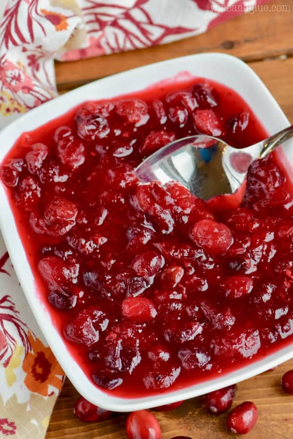 In a white dish, a spoon is digging into the Cranberry Sauce. 