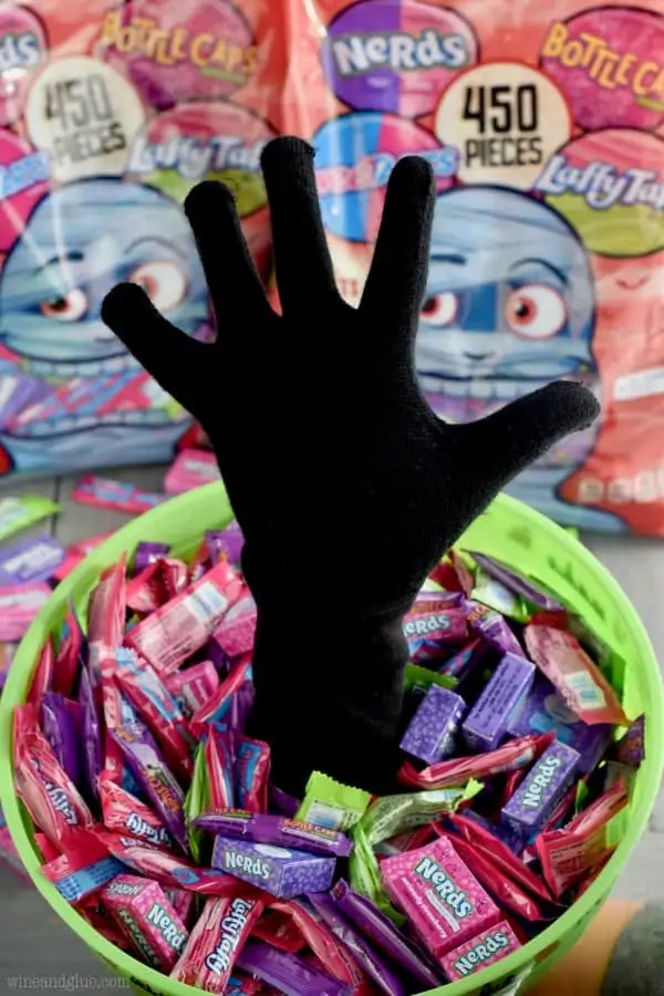 A bucket filled with Nerds and Laffy Taffy has a hand coming out of it. 