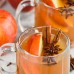 clear mug full of crockpot spiced apple cider with anise seed pods floating in it, apple slices and two cinnamon sticks