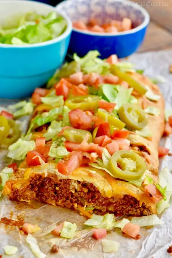 a taco braid that has been cut into and you can see the meat filling, topped with fresh tomatoes, lettuce, and jalapeños.