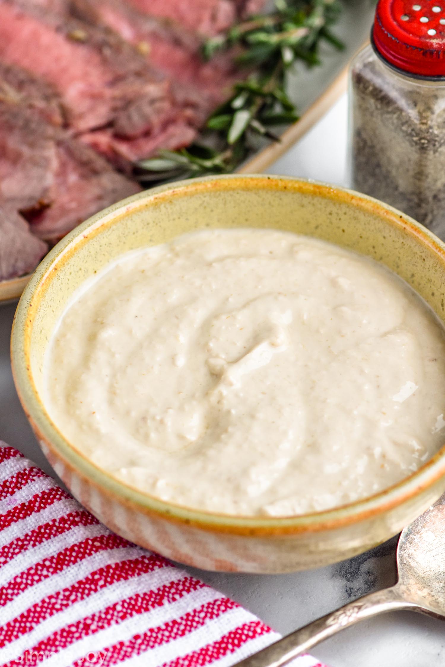 bowl of homemade horseradish sauce with platter of prime rib in background