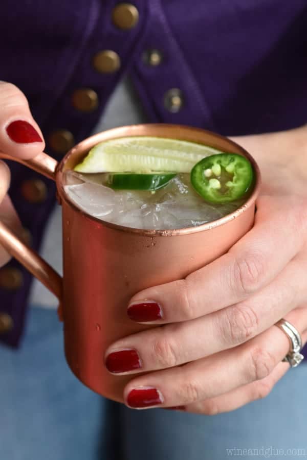 A woman holding a copper mug which has the Jalapeño Moscow mule with sliced Jalapeño and a lime