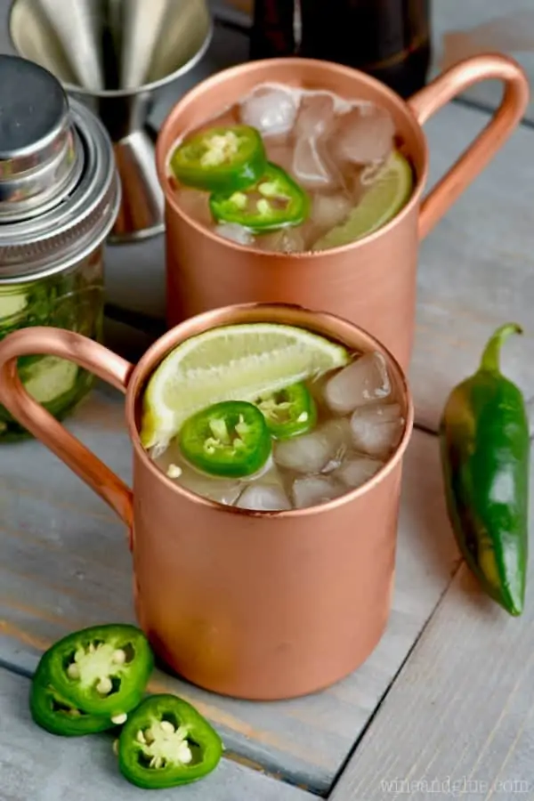 Two copper mugs filled with Jalapeño Moscow Mules with cut Jalapeño and limes. 