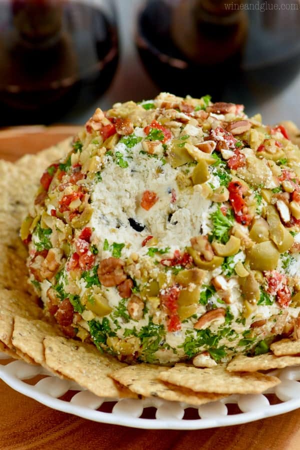 In the middle of the plate, there is an Olive Cheese Ball with a small carved out portion; surrounding the cheese ball are crackers. 