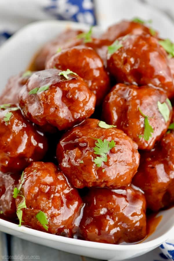 A pile of Honey BBQ Instant Pot Cocktail Meatballs on a white plate and garnished with parsley. 
