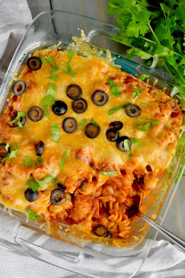 In a casserole dish, the Instant Pot Chicken Enchilada Casserole is topped with melted cheese, olives, and parsley. 