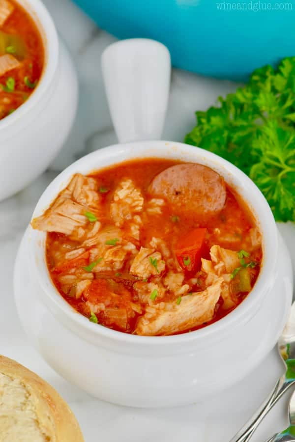 In small handle white bowls, the Jambalaya Soup has a bright red hue with shredded chicken, sausage, and more. 