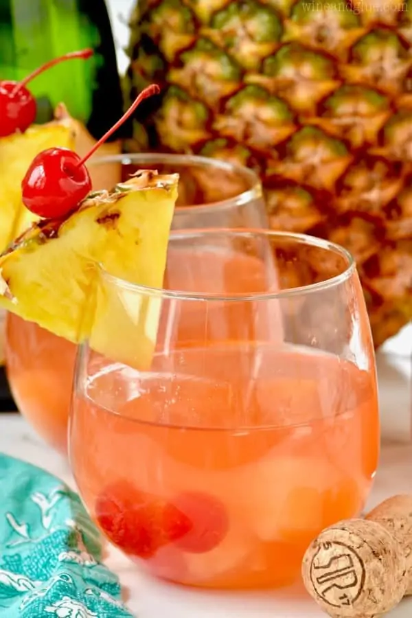 Two glasses of Pina Colada Rum Punch garnished with a slice of pineapple and a maraschino cherry.