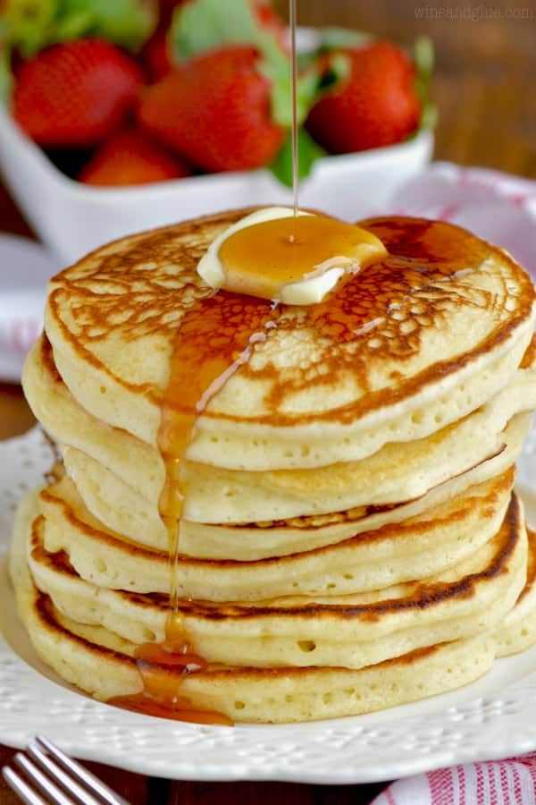 A stack of Buttermilk Pancakes with a slice of butter on top and syrup being poured on top. 