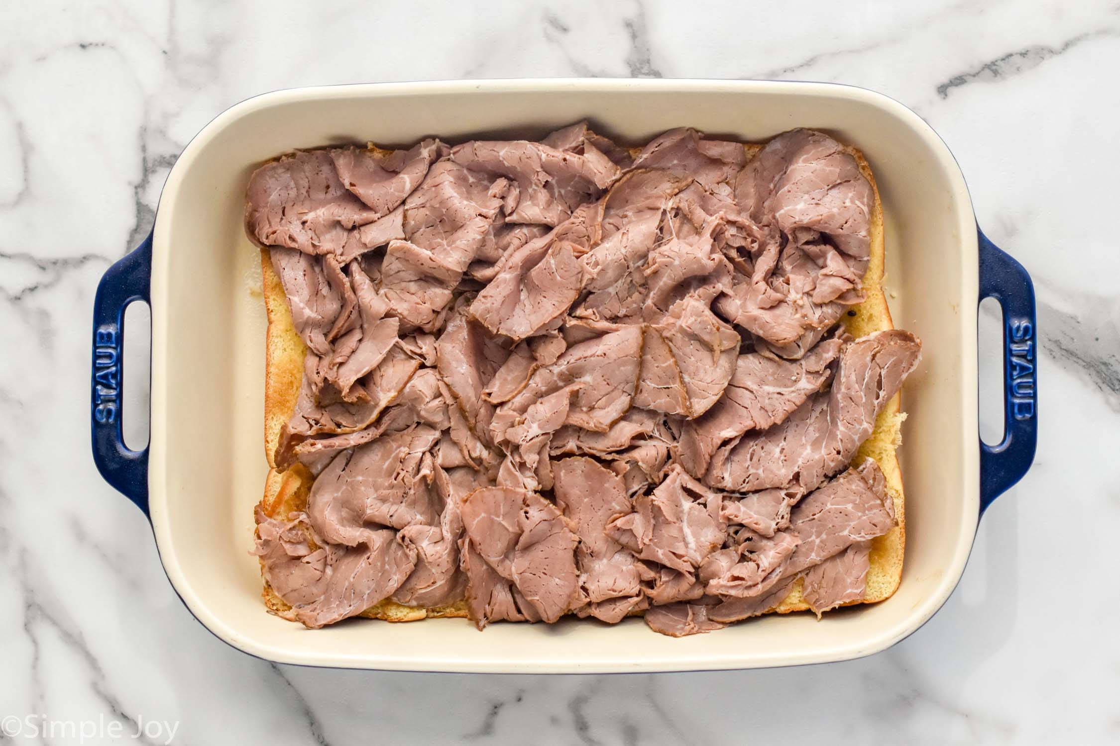 Overhead photo of baking dish of ingredients with meat on top for Philly Cheesesteak Sliders recipe.