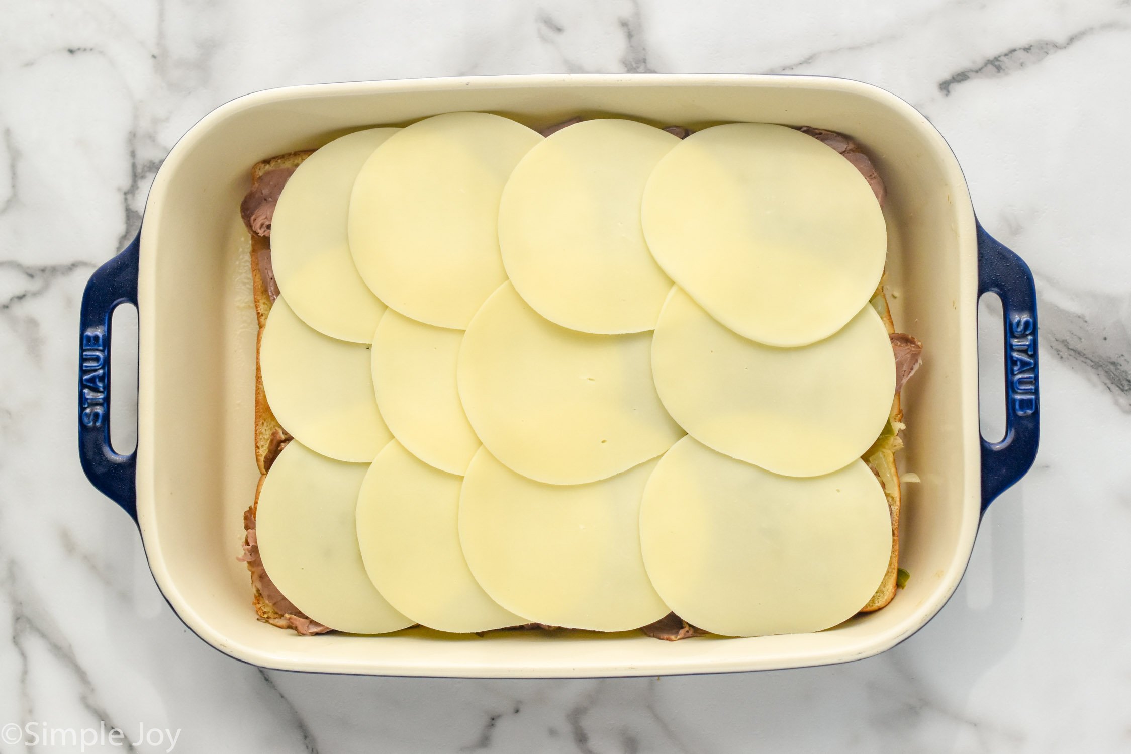 Overhead photo of a baking dish of ingredients with cheese on top of Philly Cheesesteak Sliders recipe