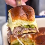 Side view of person's hand lifting Philly Cheesesteak Slider out of pan of Philly Cheesesteak Sliders.