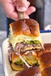 Side view of person's hand lifting Philly Cheesesteak Slider out of pan of Philly Cheesesteak Sliders.