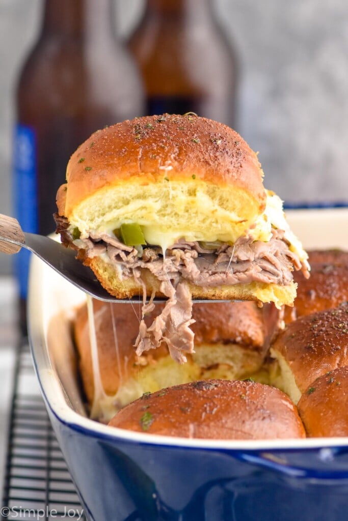 Side view of person's hand lifting Philly Cheesesteak Slider out of pan of Philly Cheesesteak Sliders.