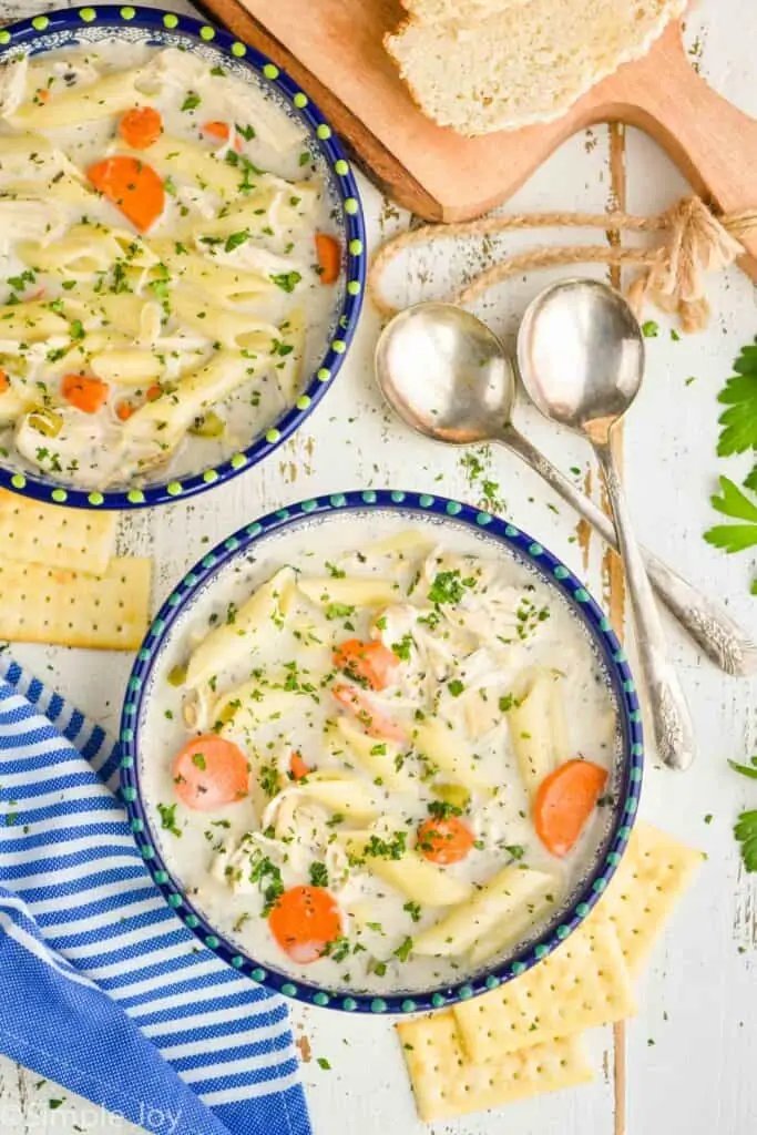 overhead view of two bowls of homemade chicken noodle soup with crackers and topped with fresh parsley