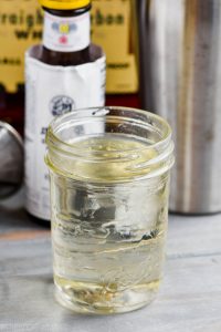 mason jar full of simple syrup with bitters and whiskey in the background
