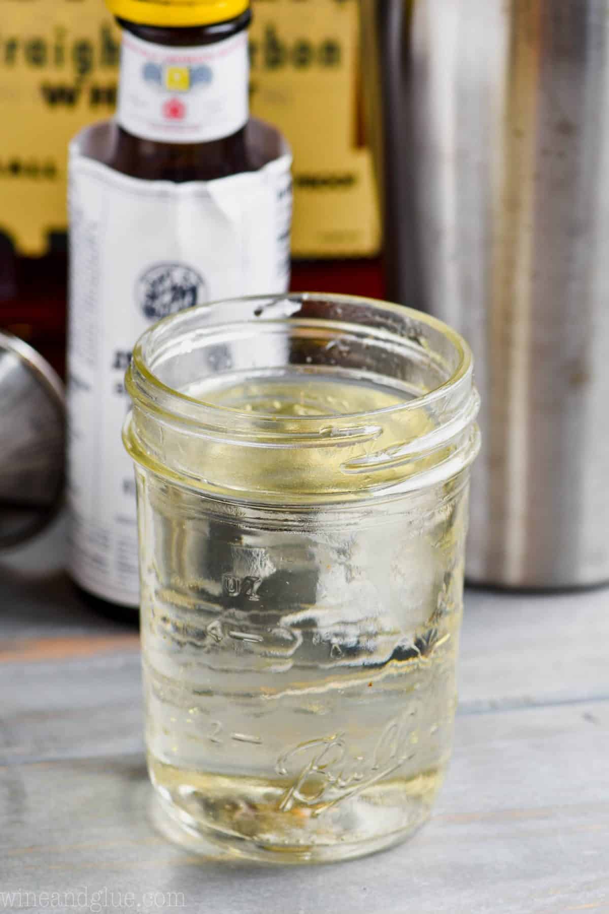 mason jar full of simple syrup with bitters and whiskey in the background