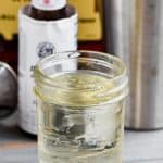 mason jar full of simple syrup with bitters and whiskey in the background