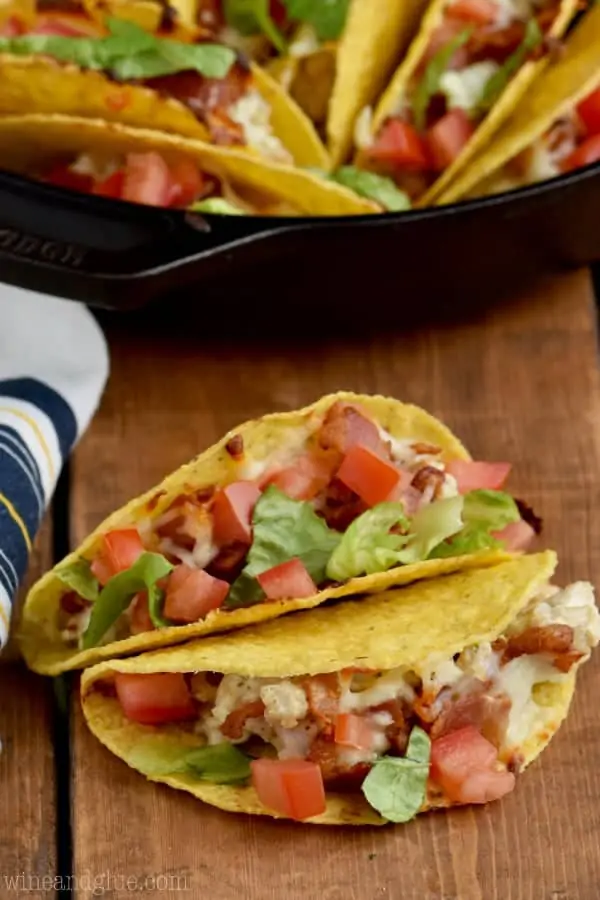 Two Creamy BLT Ranch Oven Baked Tacos are stacked on top of each other with diced tomatoes and lettuce. 
