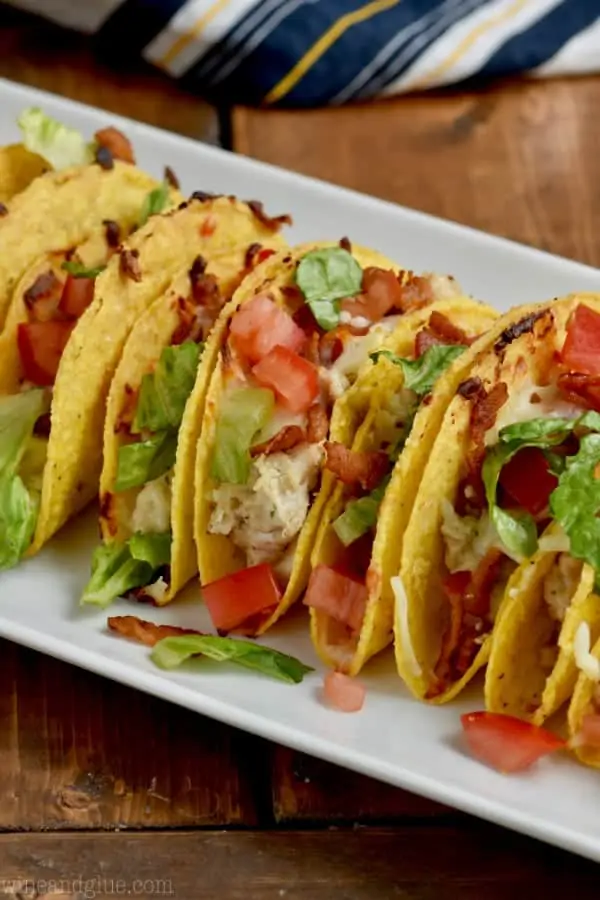 On a white dish, the Creamy BLT Ranch Oven Baked Tacos are next to each other topped with diced tomatoes and lettuce. 