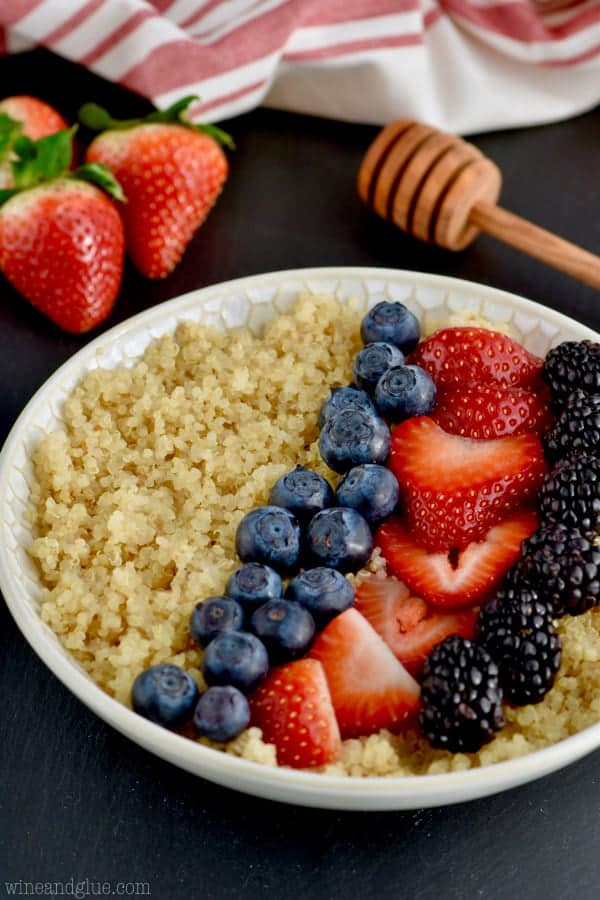 A bowl of Quinoa topped with blue berries, cut strawberries, and black berries. 