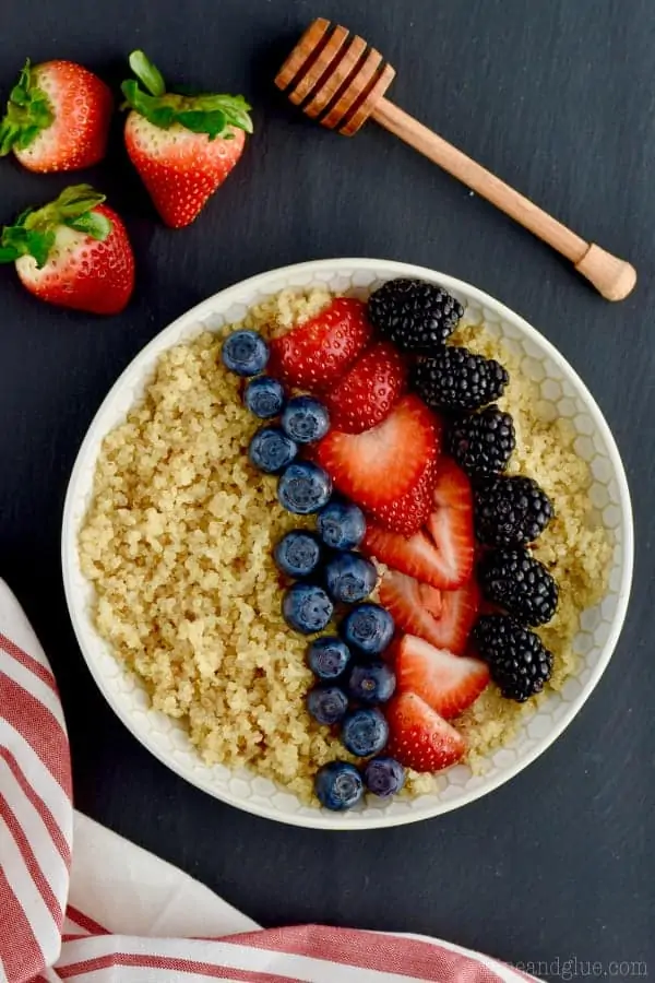 An overhead photo of a bowl of Quinoa topped with blueberries, cut strawberries, and black berries. 
