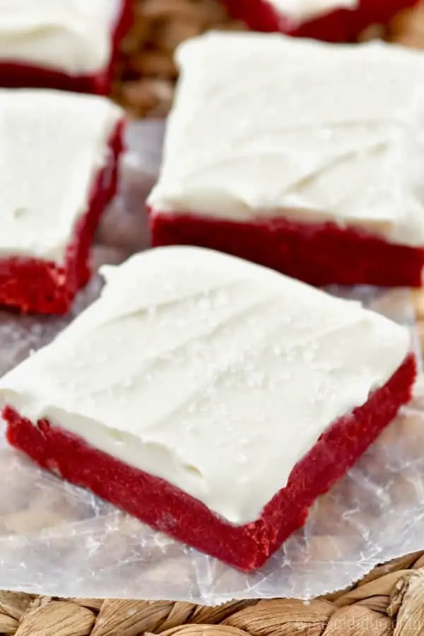 On a piece of parchment paper, the Red Velvet Bars is topped with white frosting and clear sprinkles. 