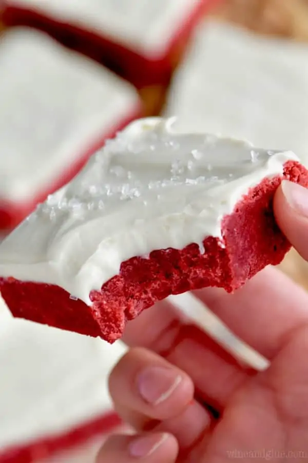 A woman holding a Red Velvet Bars topped with white frosting and clear sprinkles. 
