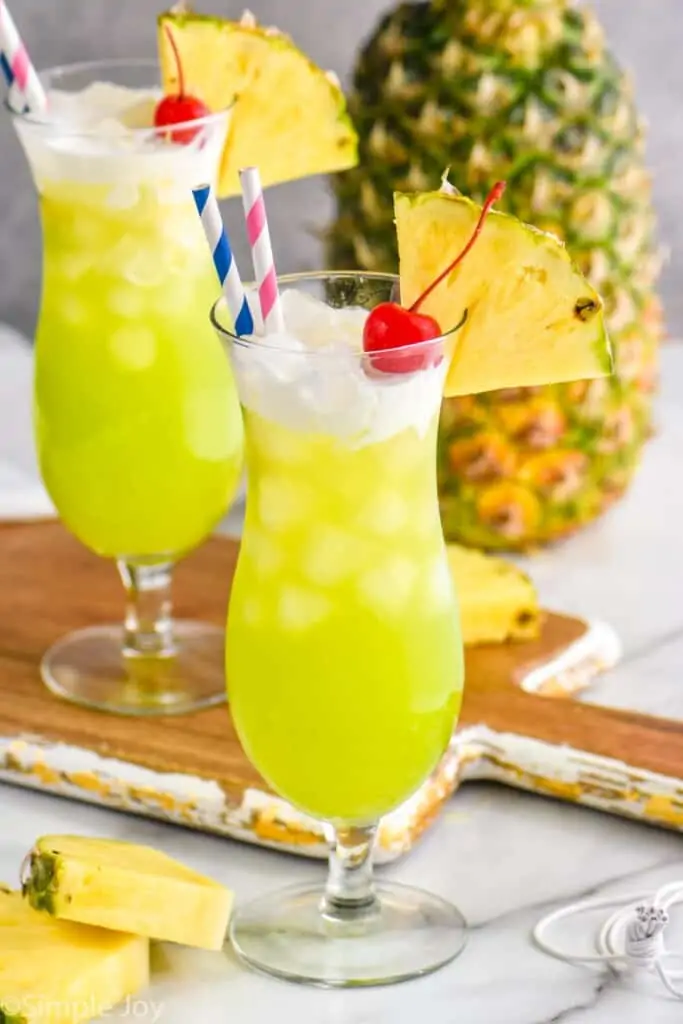 a tall glass filled with midori splice, topped with cream, garnished with a cherry and a pineapple wedge