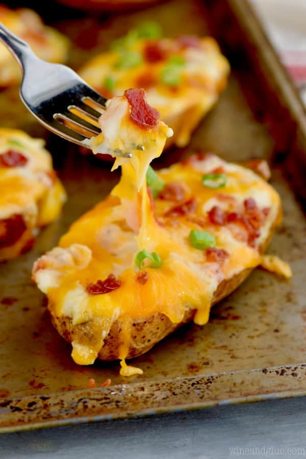On a baking sheet, the easy twice baked potato has a fork digging into it creating a cheese stretch. 
