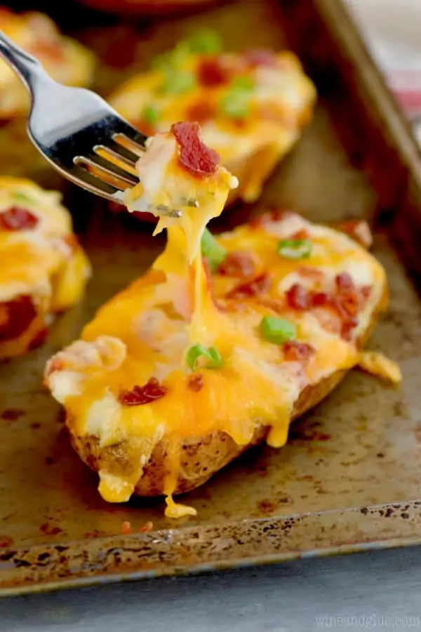 On a baking sheet, the easy twice baked potato has a fork digging into it creating a cheese stretch. 