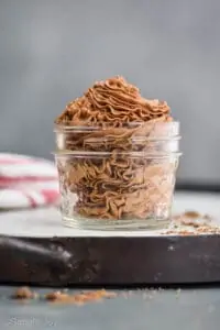 homemade chocolate whipped cream that has been piped into a small mason jar and is sitting on a white tray with chocolate shavings around it