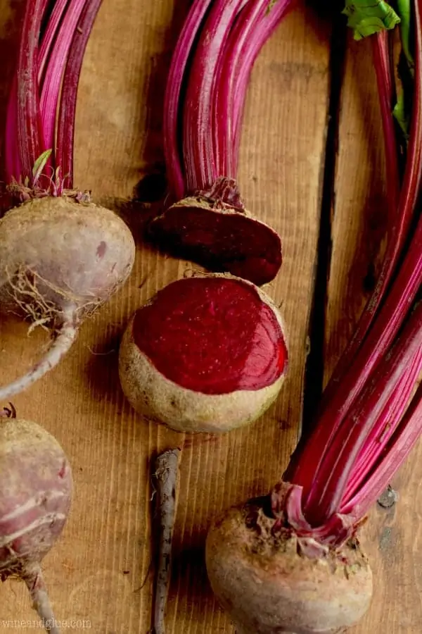 several raw beets on a wood board with the top and bottom cut off of one