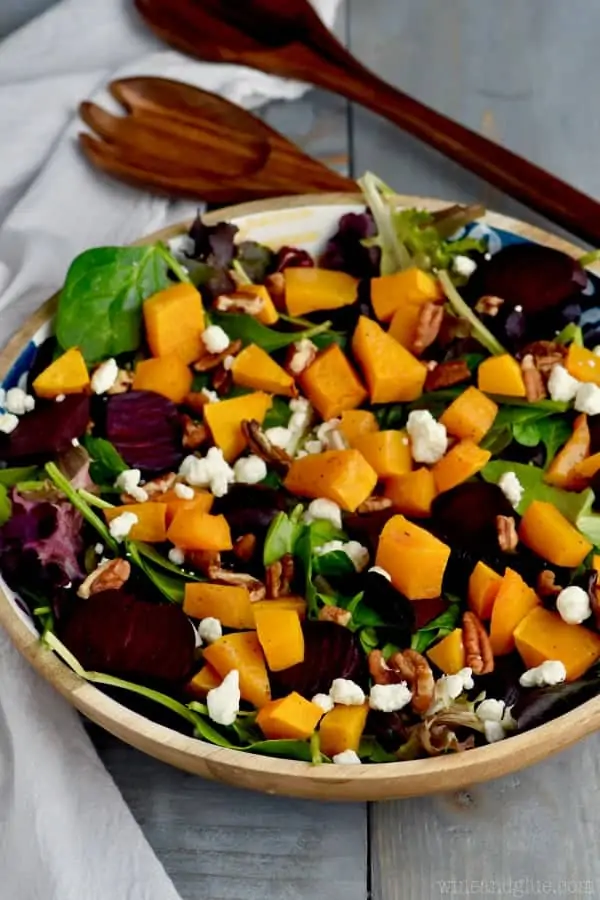 A close up photo of Roasted Beet Salad with cubbed butternut squash, pecans, goat cheese, mixed greens, and roasted beats..  