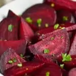 a while bowl on a wood mat filled with wedges of roasted beets sprinkled with parsley