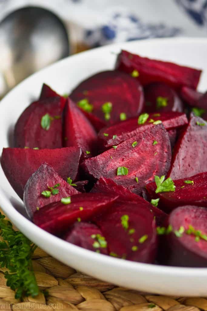 a while bowl on a wood mat filled with wedges of roasted beets sprinkled with parsley