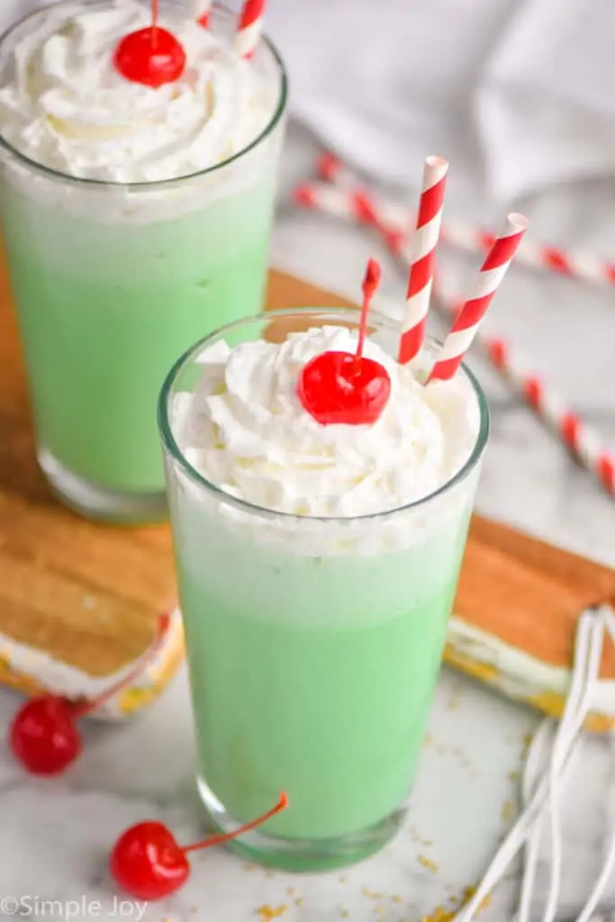 pulled back view of two tumblers filled with shamrock shake, topped with whipped cream and cherries